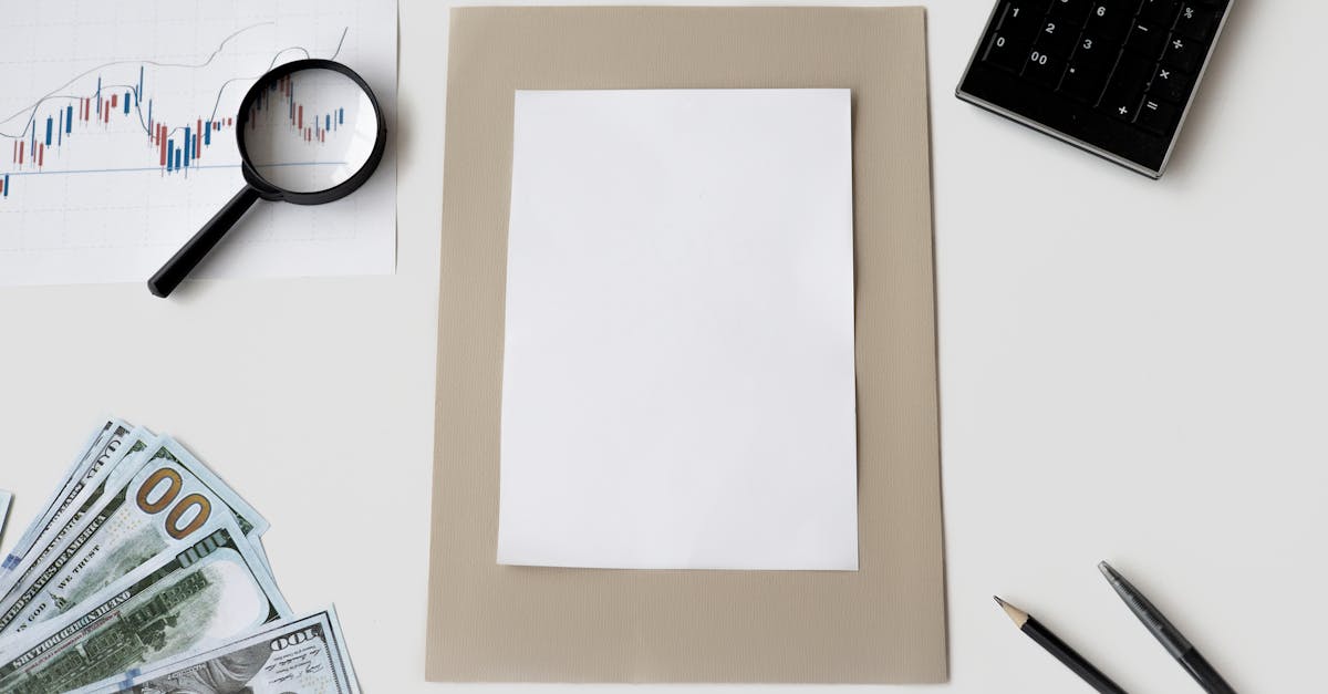 Vista superior de mesa branca com calculadora, lupa sobre gráfico financeiro, cédulas de dinheiro e papel em branco. — Foto: Hanna Pad