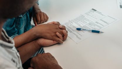 Casal de mãos dadas sobre mesa branca com formulário jurídico e caneta azul ao lado. — Foto: Kindel Media