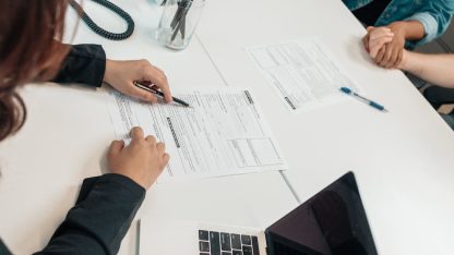 Vista superior de pessoas em uma mesa de escritório analisando e assinando documentos jurídicos. — Foto: Kindel Media
