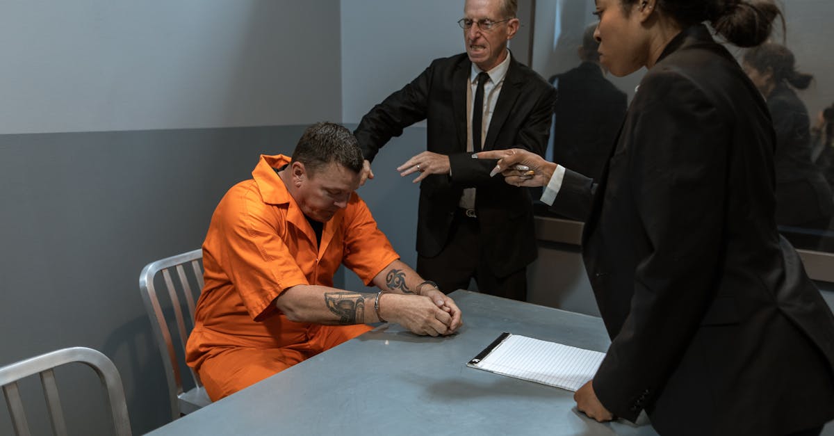 Homem em uniforme de detento sentado em sala de interrogatório com advogados ao redor discutindo documentos. — Foto: RDNE Stock project