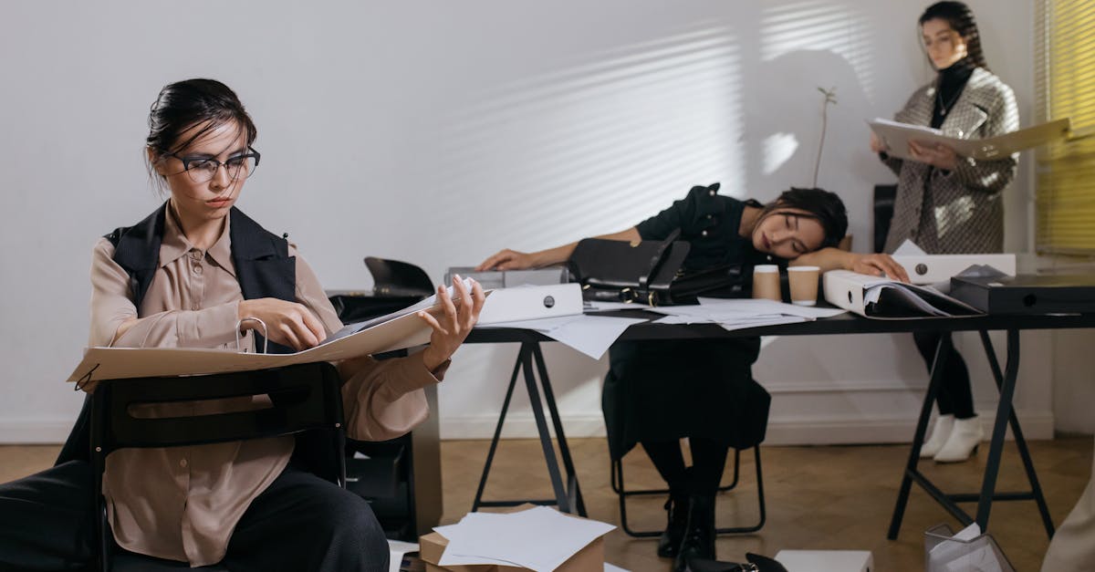 Mulheres trabalhando em escritório com documentos, uma delas dormindo sobre a mesa por exaustão. — Foto: cottonbro studio