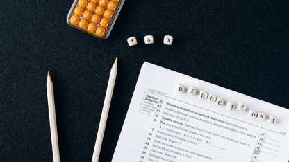 Vista superior de formulário de imposto com a palavra deductions escrita em pequenos blocos sobre a mesa preta. — Foto: Nataliya Vaitkevich