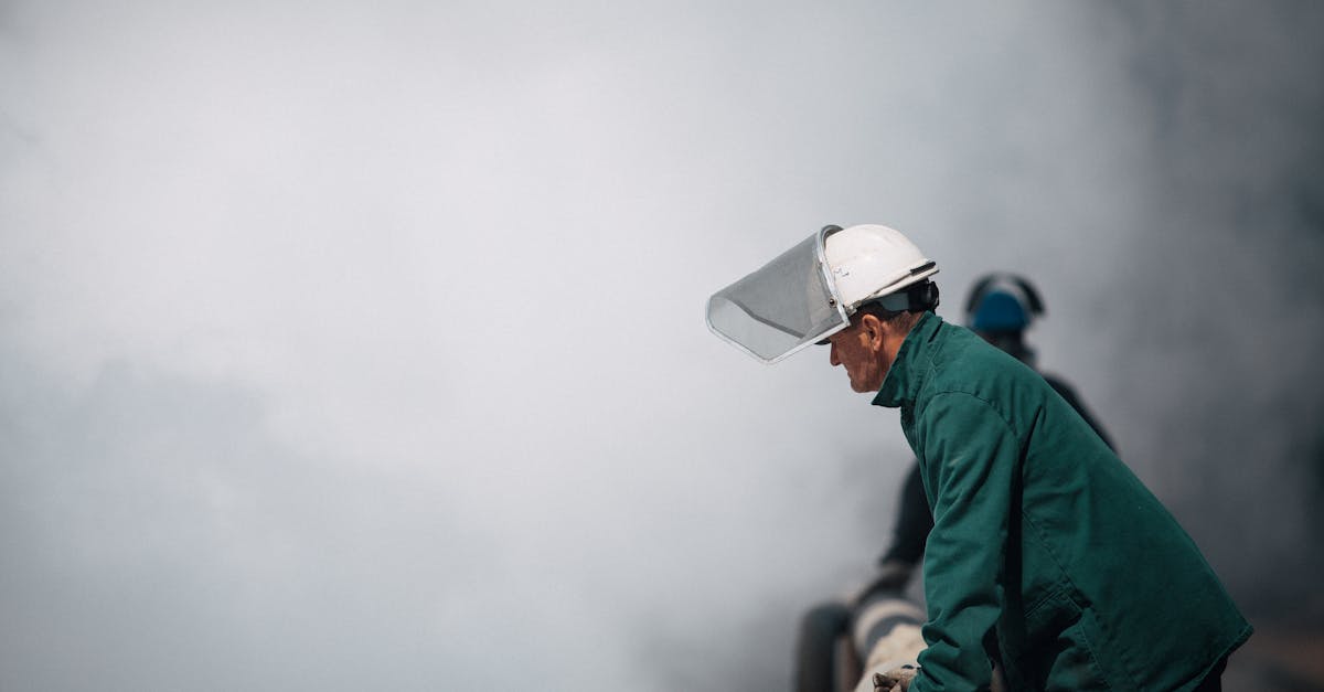 Trabalhador com capacete e protetor facial em ambiente industrial com fumaça branca ao fundo. — Foto: Bence Szemerey