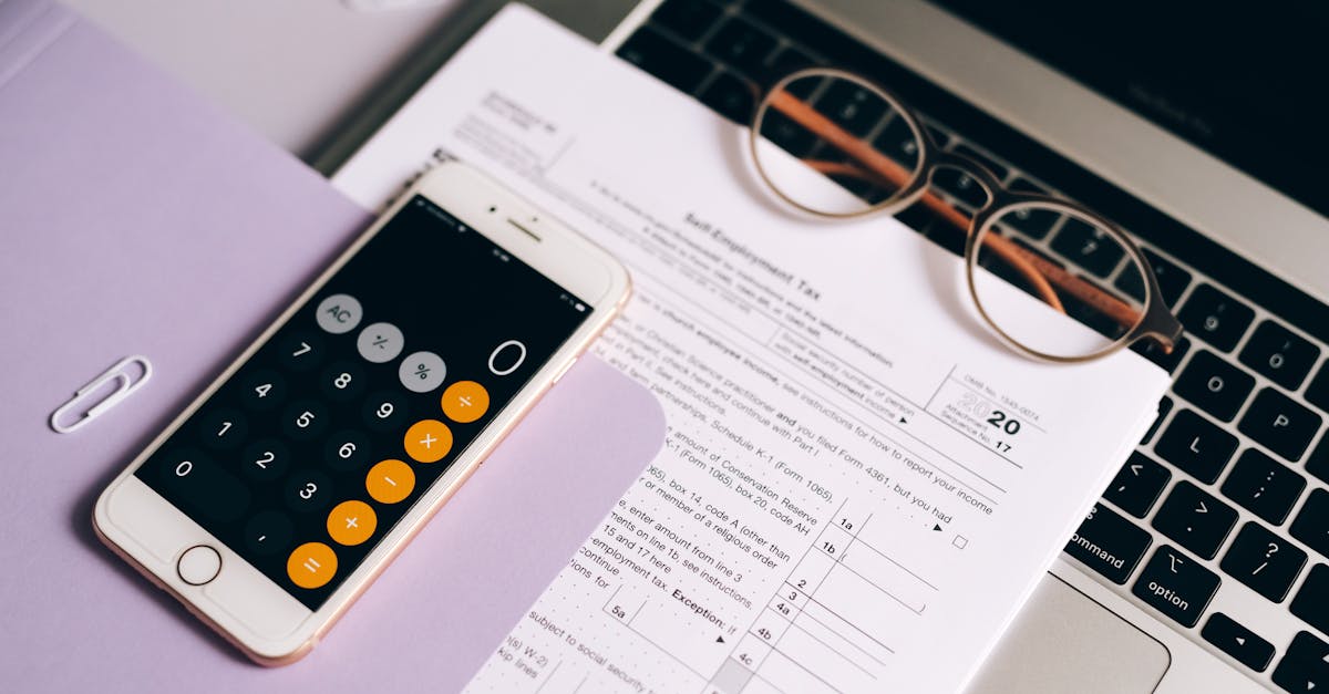 Documentos de impostos sobre um notebook com óculos e um celular exibindo uma calculadora em ambiente de escritório. — Foto: Leeloo The First