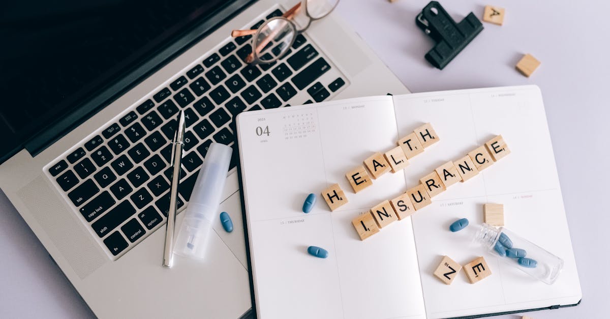 Notebook, óculos e agenda aberta com as palavras Health Insurance escritas em blocos de madeira ao lado de cápsulas. — Foto: Leeloo The First