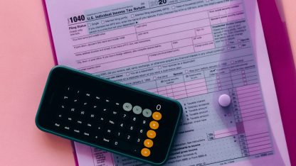 Calculadora sobre formulário de declaração de imposto de renda em uma pasta rosa. — Foto: Nataliya Vaitkevich