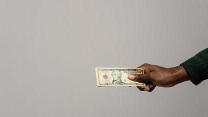 Pensao alimenticia 82086 1774796534 Mão de uma pessoa segurando uma nota de dólar contra um fundo cinza neutro. — foto: tima miroshnichenko