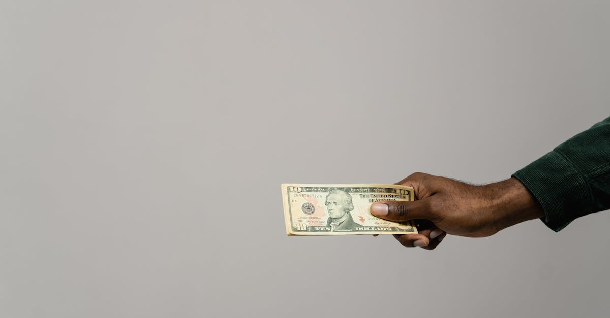 Mão de uma pessoa segurando uma nota de dólar contra um fundo cinza neutro. — foto: tima miroshnichenko