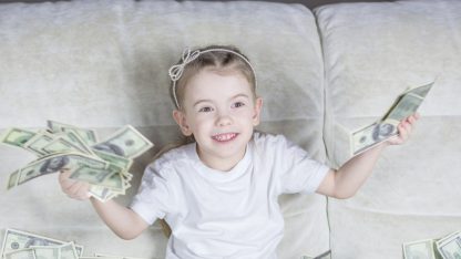 Menina sorridente sentada em um sofá segurando diversas notas de dólar. — Foto: Bermix Studio
