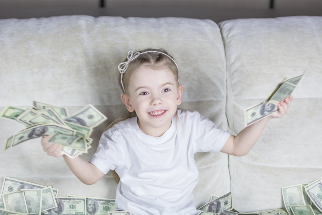 Menina sorridente sentada em um sofá segurando diversas notas de dólar. — Foto: Bermix Studio