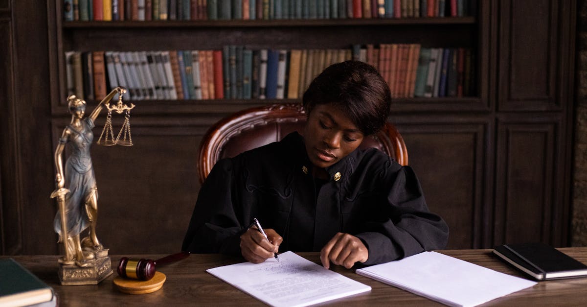 Juíza negra escrevendo em documentos em um gabinete jurídico com estante de livros e estátua da justiça ao fundo. — Foto: KATRIN BOLOVTSOVA