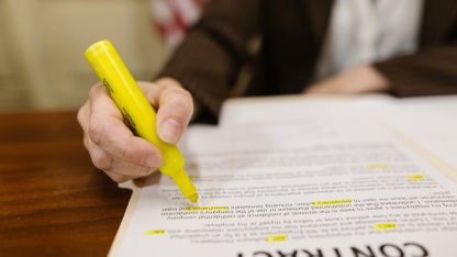 Mão de pessoa usando marca-texto amarelo em um contrato sobre uma mesa de madeira. — Foto: RDNE Stock project