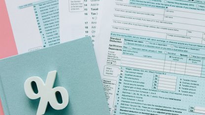 Formulários de declaração de imposto sobre uma mesa ao lado de um símbolo de porcentagem branco. — Foto: Nataliya Vaitkevich