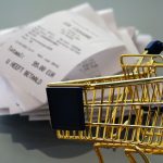 Miniatura de carrinho de compras dourado em frente a uma pilha de notas fiscais e recibos de papel. — Foto: Alexas_Fotos