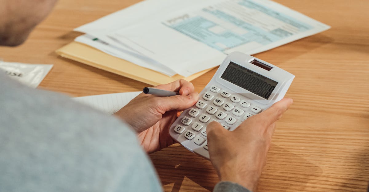 Pessoa utilizando calculadora branca e caneta para analisar documentos financeiros sobre uma mesa de madeira. — Foto: Kindel Media
