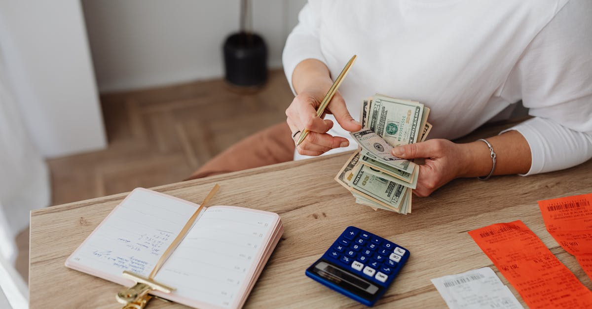Pessoa contando notas de dinheiro sobre mesa com calculadora, agenda e recibos em um ambiente de escritório. — Foto: www.kaboompics.com