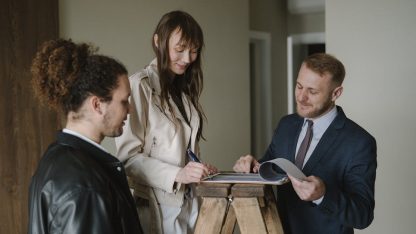 Casal assinando documentos em uma prancheta segurada por um homem de terno e gravata. — Foto: Anastasia  Shuraeva