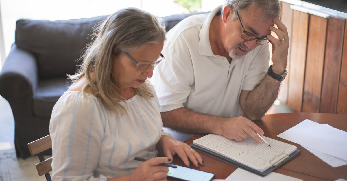 Casal de meia-idade sentado à mesa analisando papéis e documentos com semblante sério e preocupado. — Foto: Kampus Production