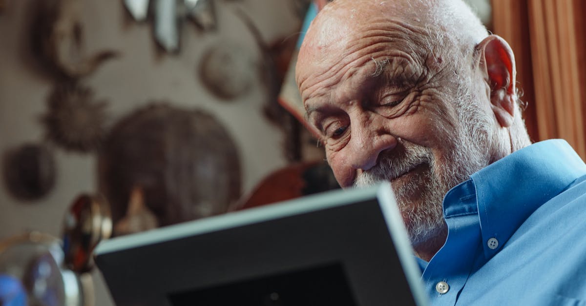 Homem idoso sorridente com barba grisalha olhando para um porta-retrato em ambiente interno iluminado. — Foto: Kindel Media
