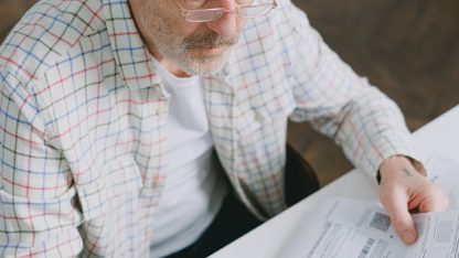 Homem idoso de óculos e camisa xadrez analisando papéis e documentos sobre uma mesa branca. — Foto: SHVETS production