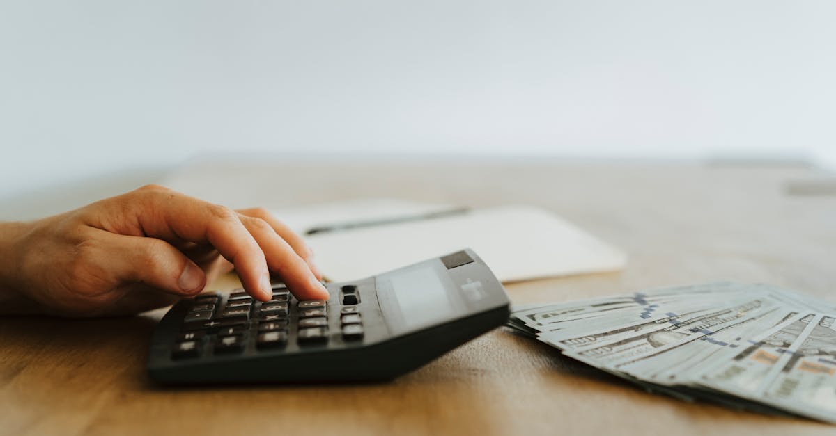 Mão de uma pessoa utilizando uma calculadora sobre uma mesa de madeira com notas de dinheiro e um caderno ao fundo. — Foto: olia danilevich