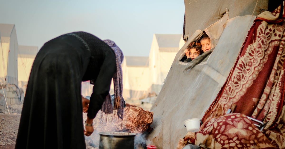 Mulher cozinha em acampamento enquanto crianças observam de dentro de uma tenda em campo de refugiados. — Foto: Ahmed akacha