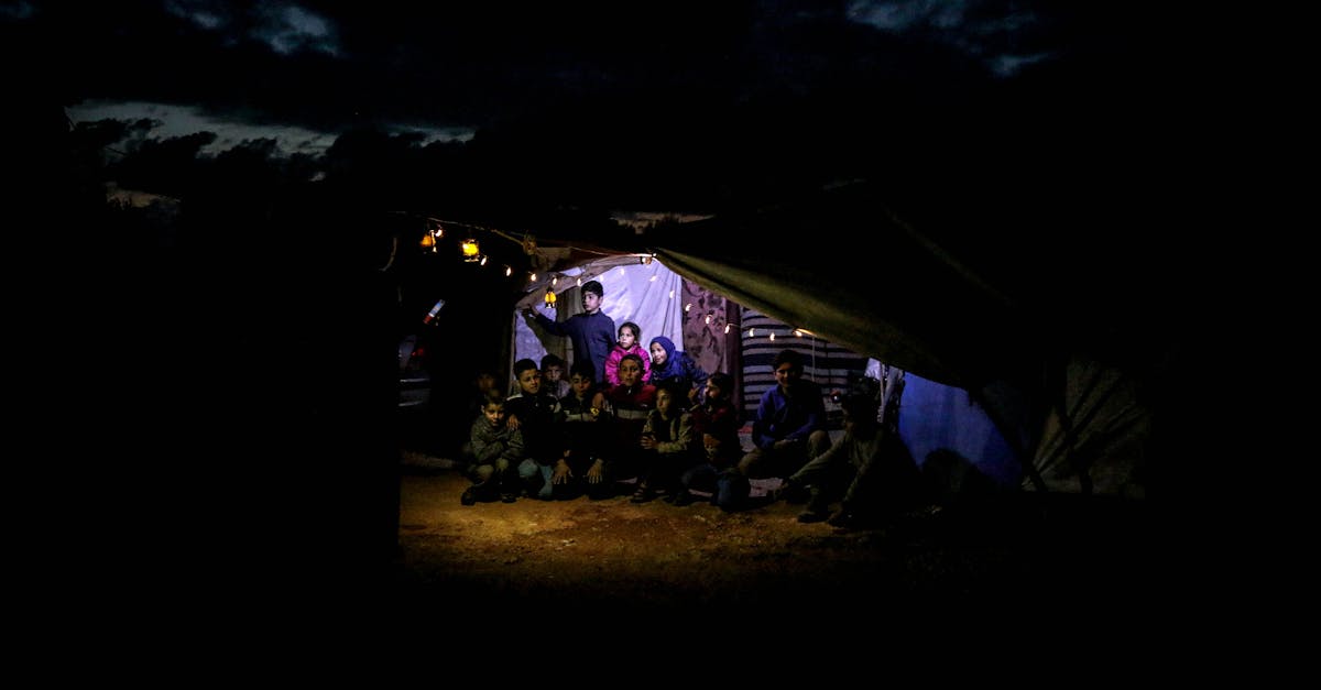 Grupo de pessoas refugiadas abrigadas em uma tenda improvisada durante a noite com iluminação interna. — Foto: Ahmed akacha