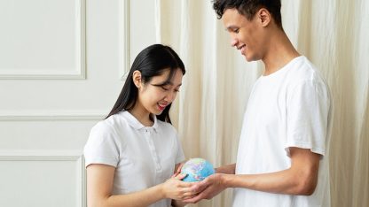 Um homem e uma mulher de diferentes etnias seguram juntos um pequeno globo terrestre em um ambiente claro. — Foto: Mikhail Nilov