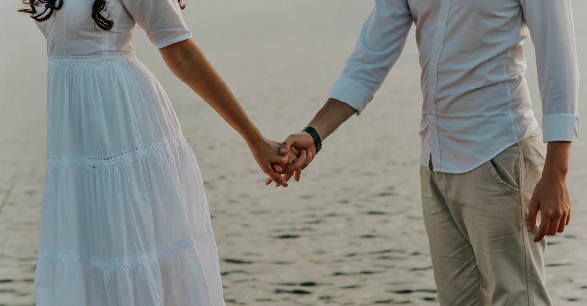 Close de um casal de mãos dadas em frente ao mar, vestindo roupas brancas leves. — Foto: Icaro Breno