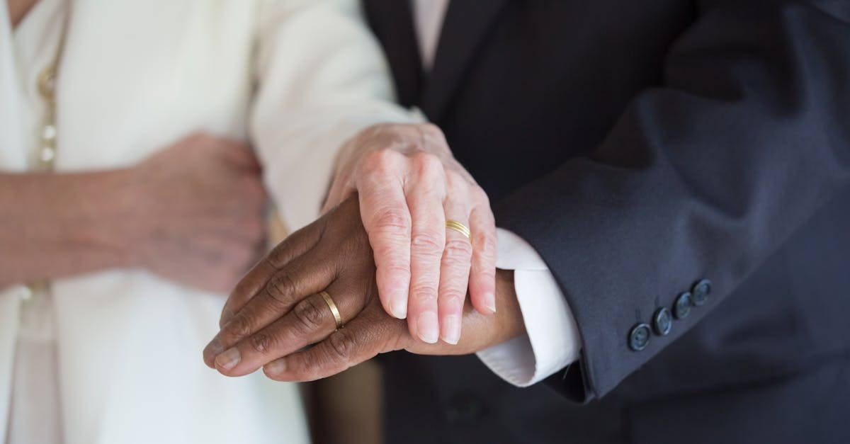 Close das mãos de um casal com alianças, um homem negro de terno e uma mulher branca vestida de noiva. — Foto: Kampus Production