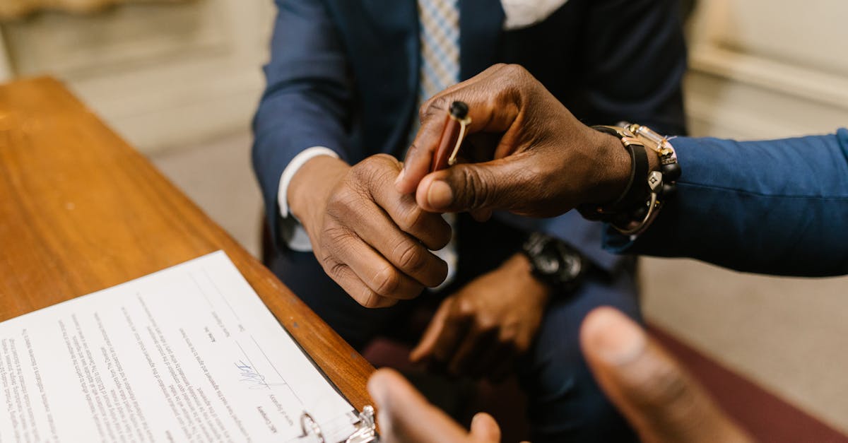 Close de mãos entregando uma caneta para assinatura de contrato sobre uma mesa de madeira. — Foto: RDNE Stock project