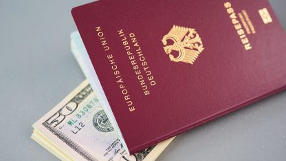 Passaporte europeu bordô sobre um maço de notas de dólares americanos em fundo cinza. — Foto: webandi
