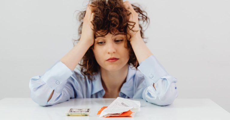 Mulher com as mãos na cabeça demonstrando preocupação ao olhar para contas e notas de dinheiro sobre a mesa. — Foto: www.kaboompics.com