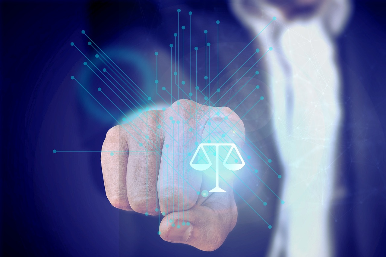 Mão de um profissional apontando para um ícone digital da balança da justiça com linhas tecnológicas ao fundo. — Foto: herbinisaac