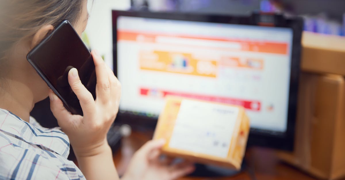 Mulher ao telefone segurando caixa de encomenda em frente a um computador com site de compras aberto. — Foto: saravut vanset