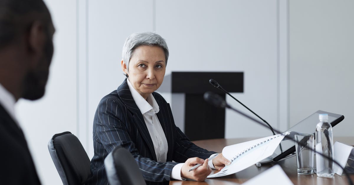 Mulher de terno em uma mesa de conferência com microfones, segurando documentos durante uma reunião profissional. — Foto: Werner Pfennig