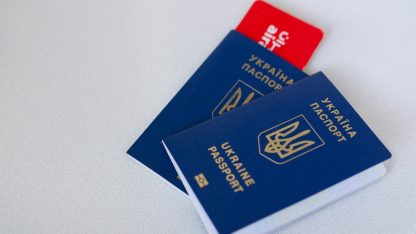 Dois passaportes azuis da Ucrânia sobre uma superfície branca com um cartão vermelho ao fundo. — Foto: Borys Zaitsev