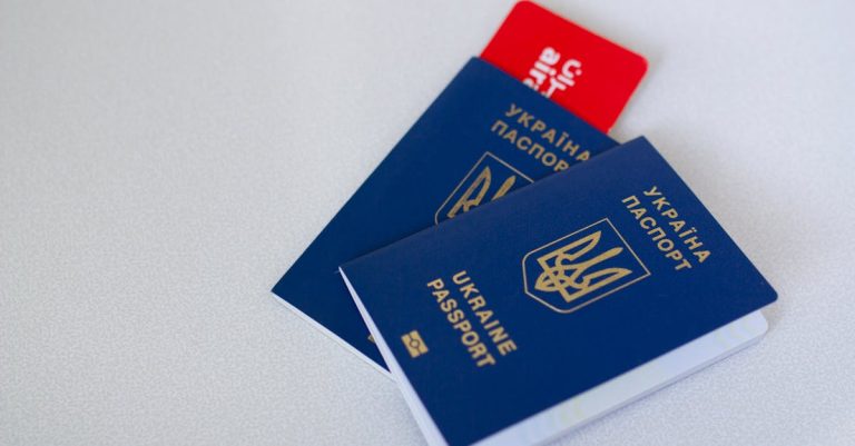 Dois passaportes azuis da Ucrânia sobre uma superfície branca com um cartão vermelho ao fundo. — Foto: Borys Zaitsev