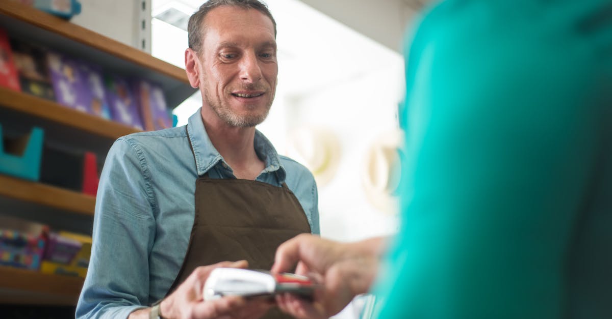 Vendedor sorridente em uma loja segurando uma máquina de cartão enquanto um cliente realiza o pagamento. — Foto: Kampus Production