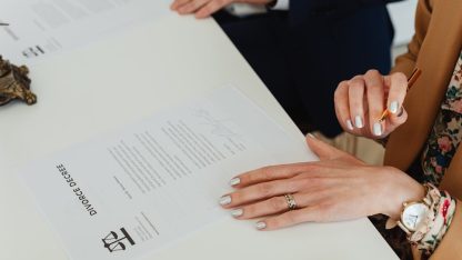 Mãos de uma mulher sobre um documento de decreto de divórcio em uma mesa branca com caneta e estátua da justiça. — Foto: www.kaboompics.com