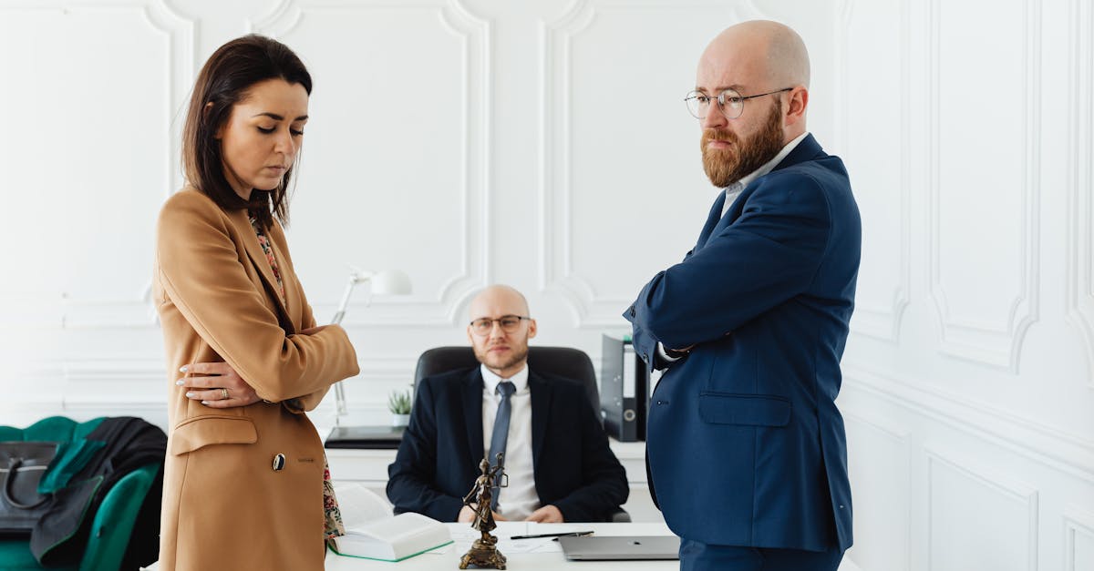 Homem e mulher de braços cruzados em clima de tensão diante de um advogado em um escritório branco. — Foto: www.kaboompics.com