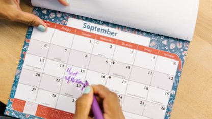Mão de uma pessoa marcando datas com uma caneta roxa em um calendário de mesa sobre uma superfície de madeira. — Foto: RDNE Stock project
