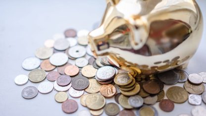 Cofrinho de porquinho dourado sobre uma pilha de moedas diversas em uma superfície clara. — Foto: Atlantic Ambience