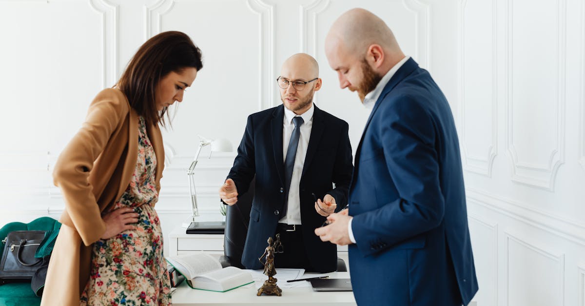 Advogado de terno conversando com casal em escritório branco com livros e estátua da justiça sobre a mesa. — Foto: www.kaboompics.com