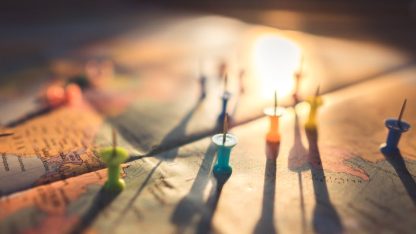 Mapa mundi com alfinetes coloridos marcando diferentes localizações sob luz solar suave. — Foto: Aksonsat Uanthoeng