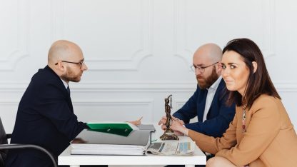 Três advogados em uma reunião de negócios ao redor de uma mesa branca com documentos e uma pequena estátua da justiça. — Foto: www.kaboompics.com