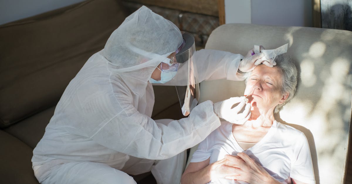 Profissional de saúde com traje de proteção realizando atendimento médico em uma senhora idosa em domicílio. — Foto: Kampus Production