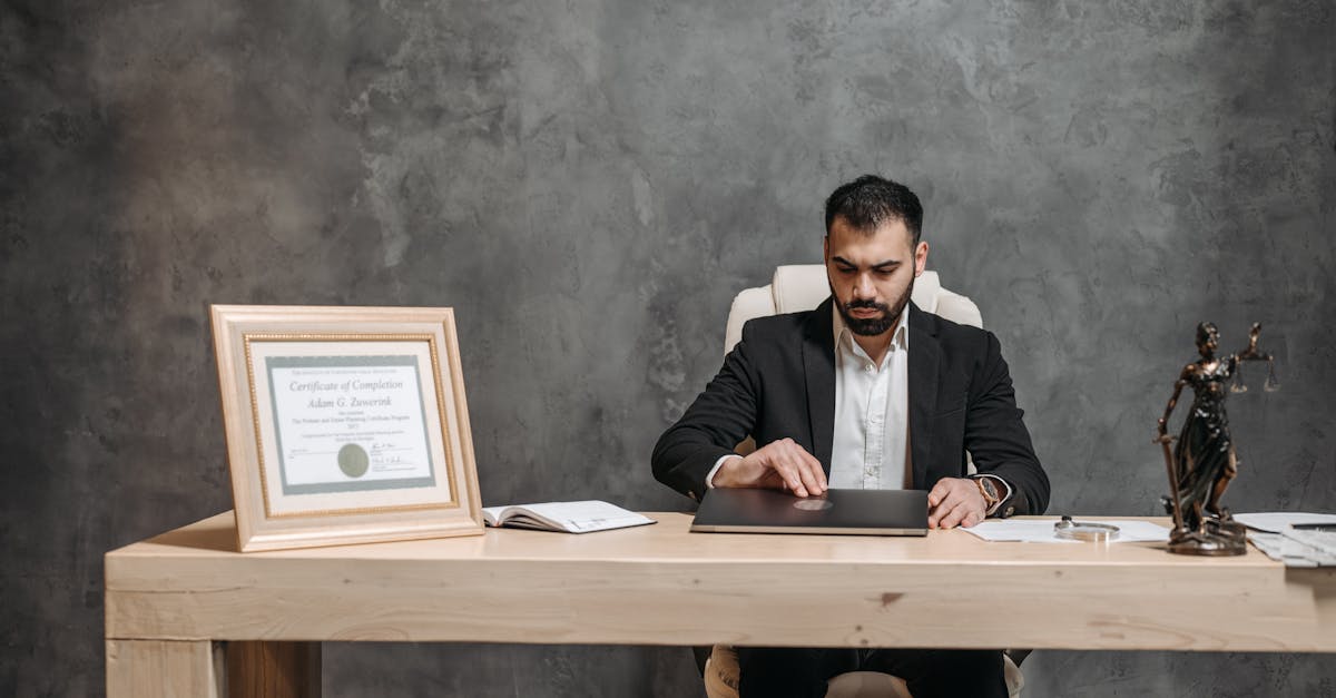 Advogado sentado à mesa de escritório com diploma emoldurado e estátua da deusa da justiça ao lado. — Foto: Pavel Danilyuk