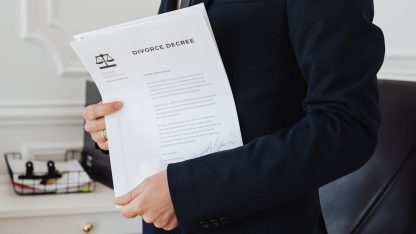 Pessoa de terno segurando papéis com o título Divorce Decree e o símbolo da balança da justiça. — Foto: www.kaboompics.com