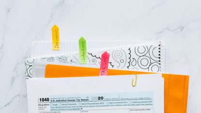Documentos de declaração de imposto com etiquetas coloridas organizados sobre uma mesa de mármore branca. — Foto: Nataliya Vaitkevich